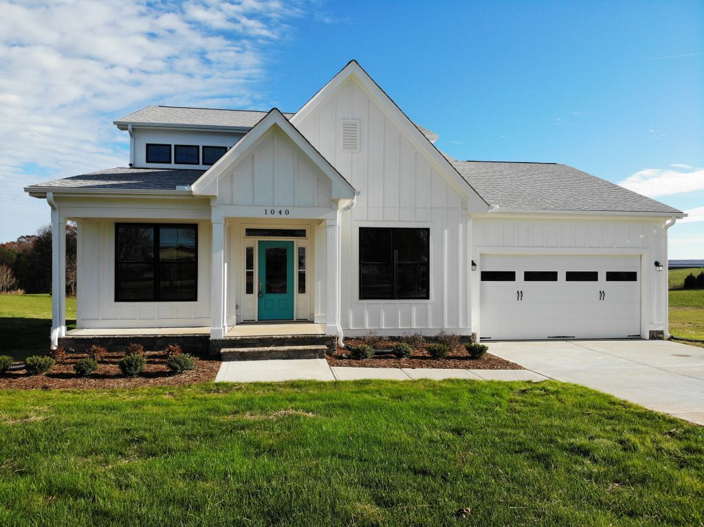 Dutch Quality Quail Ridge Gray Weatherledge stone accents, board and batt exterior painted in Sherwin Williams SW-7005 Pure White, with door in Benjamin Moore Peacock Blue 2049-40, constructed by custom home builder Travars Built Homes near Pittsboro NC