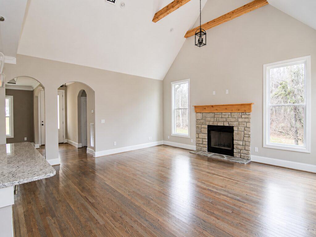Spacious family great room featuring a soaring vaulted ceiling with exposed natural wood beams, a floor-to-ceiling stone veneer fireplace with a wood mantel, and arched doorways over oak hardwood flooring.