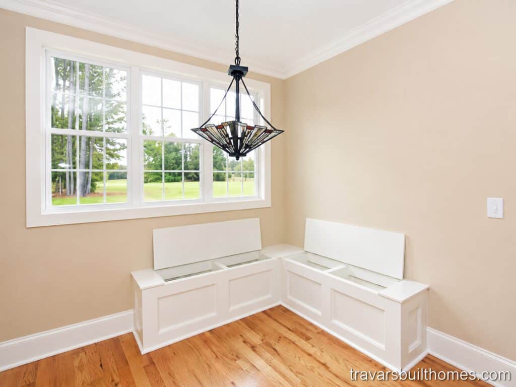 Cozy breakfast nook and casual kitchen dining area highlighting natural wood flooring, a custom L-shaped corner bench with integrated storage seating, and a geometric stained-glass chandelier.