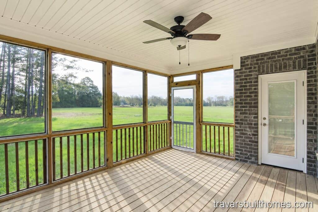 Custom screened-in back porch designed for outdoor living, featuring natural wood railings and support posts, a white beadboard ceiling with a fan, a brick accent wall, and expansive views of a green field.
