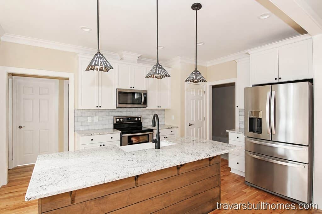 Custom kitchen layout showcasing white perimeter cabinets, a light gray subway tile backsplash, stainless steel appliances, and a large wood-paneled kitchen island with a speckled stone countertop.