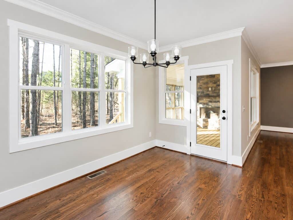 Bright morning room featuring a modern black glass-shade chandelier, deep oak flooring, and a clear glass back door that reveals a stacked stone fireplace on the covered porch, crafted by Travars Built Homes.