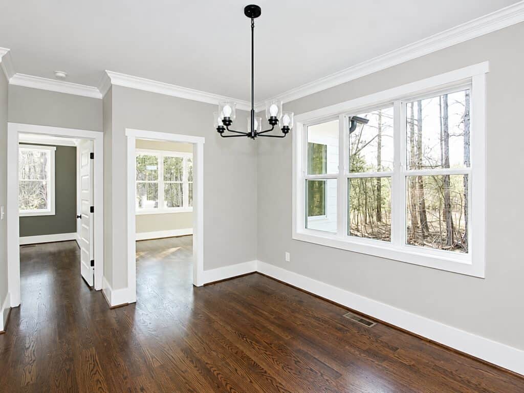 Sunlit breakfast area or informal dining space featuring continuous hardwood floors, soft greige walls, and open transitions leading to hallways and adjacent rooms, designed by Travars Built Homes.