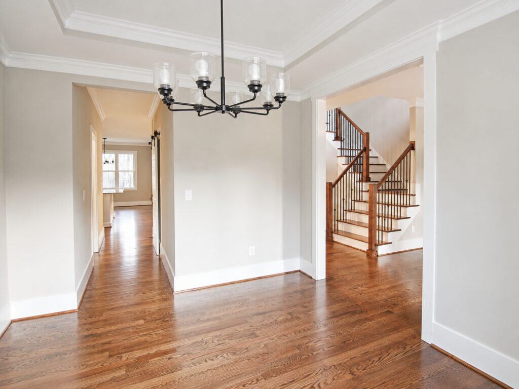 Elegant formal dining room highlighting an iron candelabra chandelier and a clear view through a wide archway to a grand wood-and-iron staircase in the front foyer, built by Travars Built Homes.