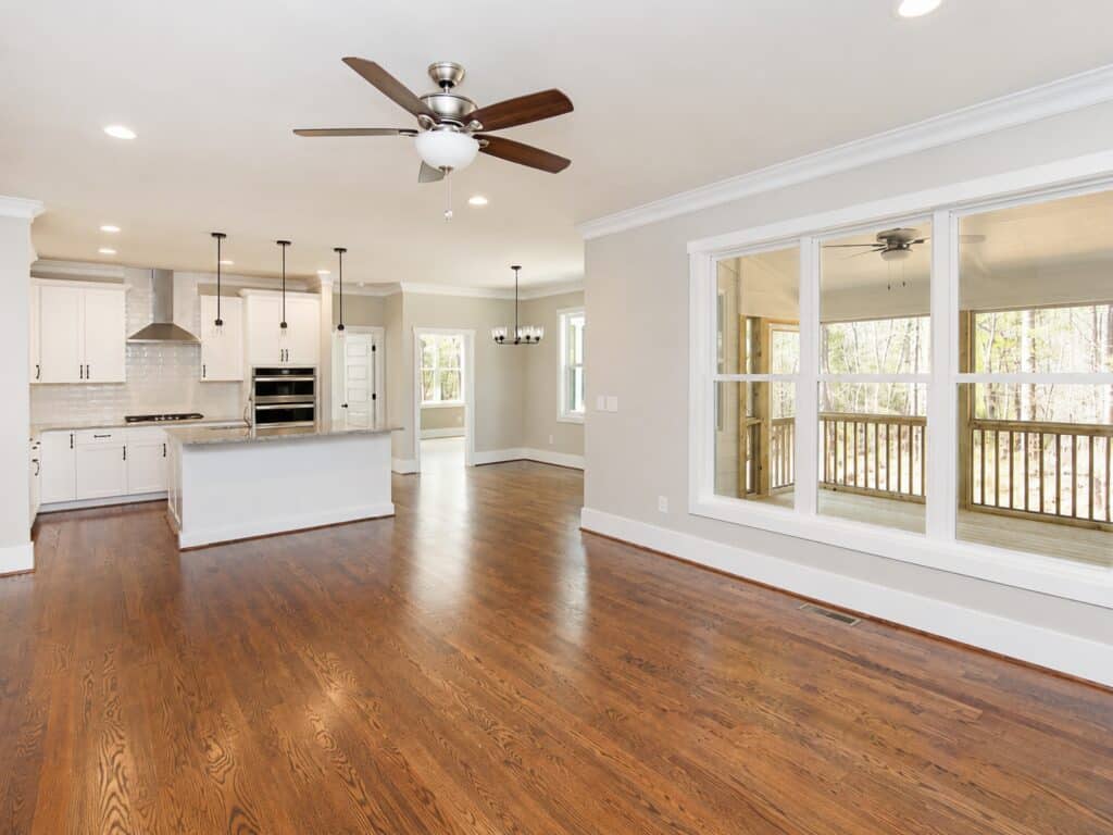 Open-concept main level showcasing a spacious living area that flows effortlessly into a custom kitchen with white cabinetry, a center island, and rich hardwood flooring, designed by Travars Built Homes.