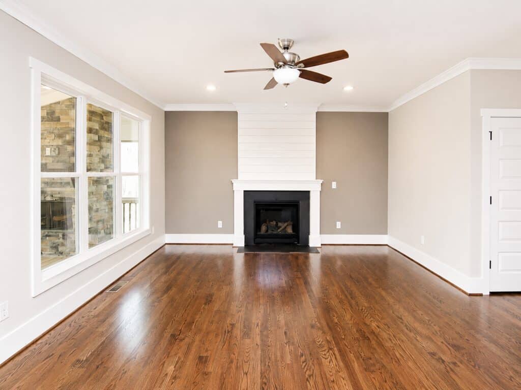 Custom living room featuring a classic black fireplace surrounded by a crisp white mantel and a matching white shiplap overmantel, set against warm oak hardwood floors, built by Travars Built Homes.