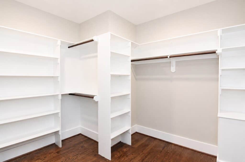 Spacious primary walk-in closet detailing extensive built-in white shelving towers, dual-level wooden hanging rods, and a warm hardwood floor, crafted by Travars Built Homes.