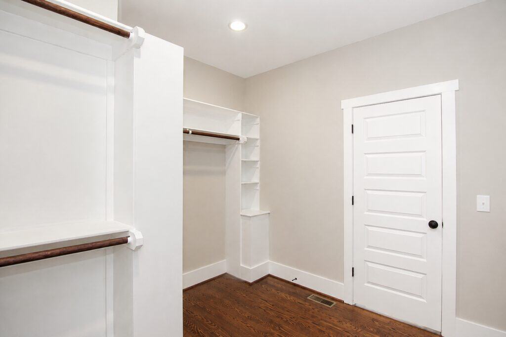 Alternative angle of the walk-in closet highlighting custom built-in white laminate shelving units and a solid white door leading back out to the master suite hallway, built by Travars Built Homes.