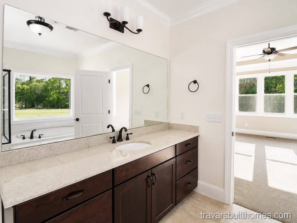 Elegant en-suite bathroom view focusing on a long dark espresso double vanity with a polished light quartz countertop, contemporary black hardware, and an expansive seamless wall mirror, designed by Travars Built Homes.