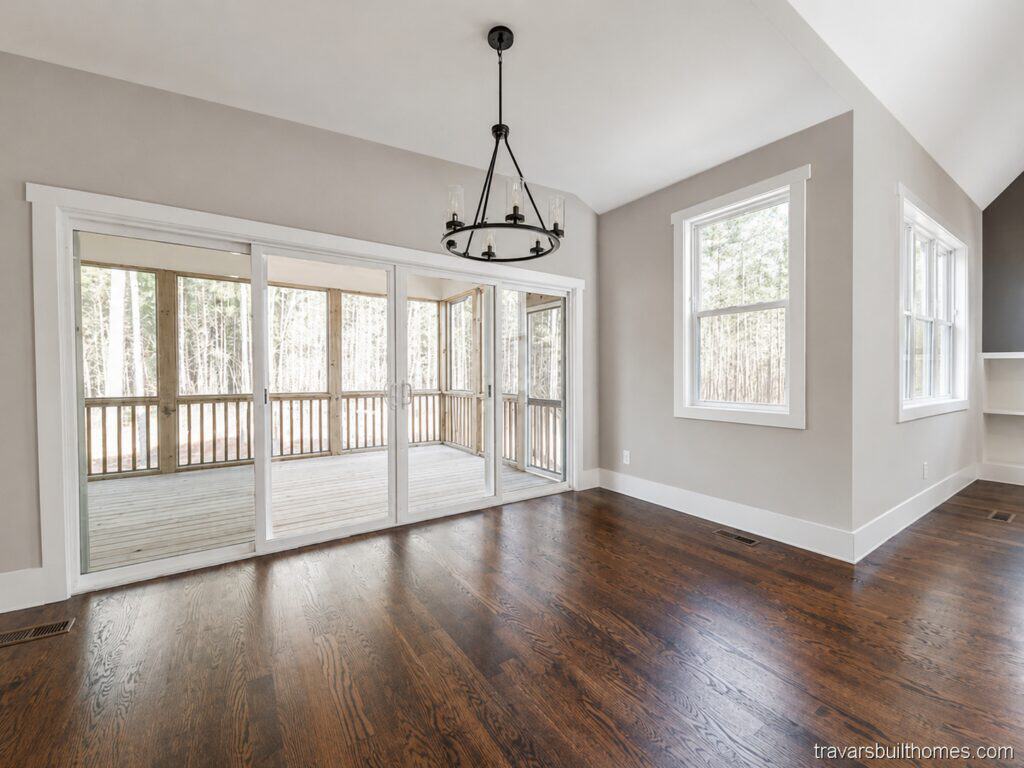 Beautiful custom breakfast nook or dining area showcasing a sleek black ring chandelier, rich dark oak floors, and large glass sliding doors that open to the screened-in back porch, built by Travars Built Homes.