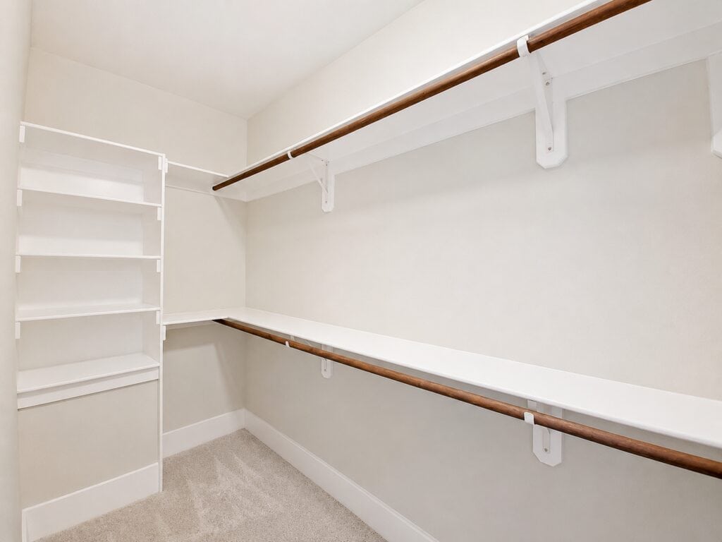 Spacious primary walk-in closet featuring extensive built-in white organization towers, dual-level hanging rods, and comfortable plush carpeting, crafted by Travars Built Homes.