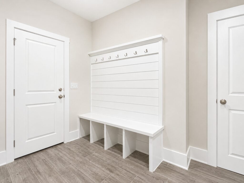 Functional custom mudroom hallway highlighting a built-in white drop zone bench with lower cubbies, a shiplap back panel, and dark coat hooks, crafted by Travars Built Homes.
