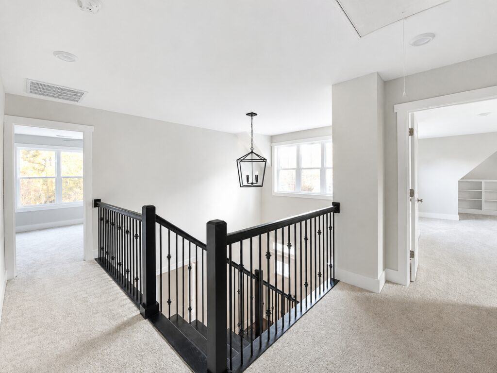 Wide view of a custom upstairs landing and staircase overlook featuring a striking black wood-and-iron railing, light grey walls, and a modern black lantern pendant light, designed by Travars Built Homes.