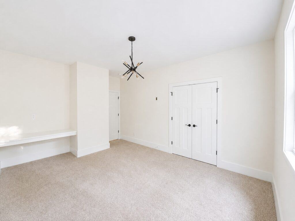 Bright custom guest bedroom or flex space featuring crisp white walls, a built-in floating desk nook, a modern sputnik-style chandelier, and double closet doors, built by Travars Built Homes.