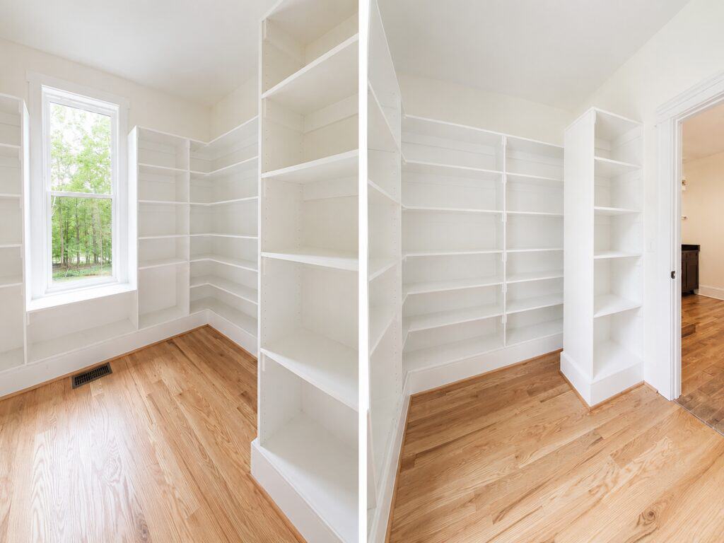 Split perspective of a spacious custom walk-in closet featuring floor-to-ceiling white built-in shelving, wooden hanging rods, and warm hardwood flooring, built by Travars Built Homes.