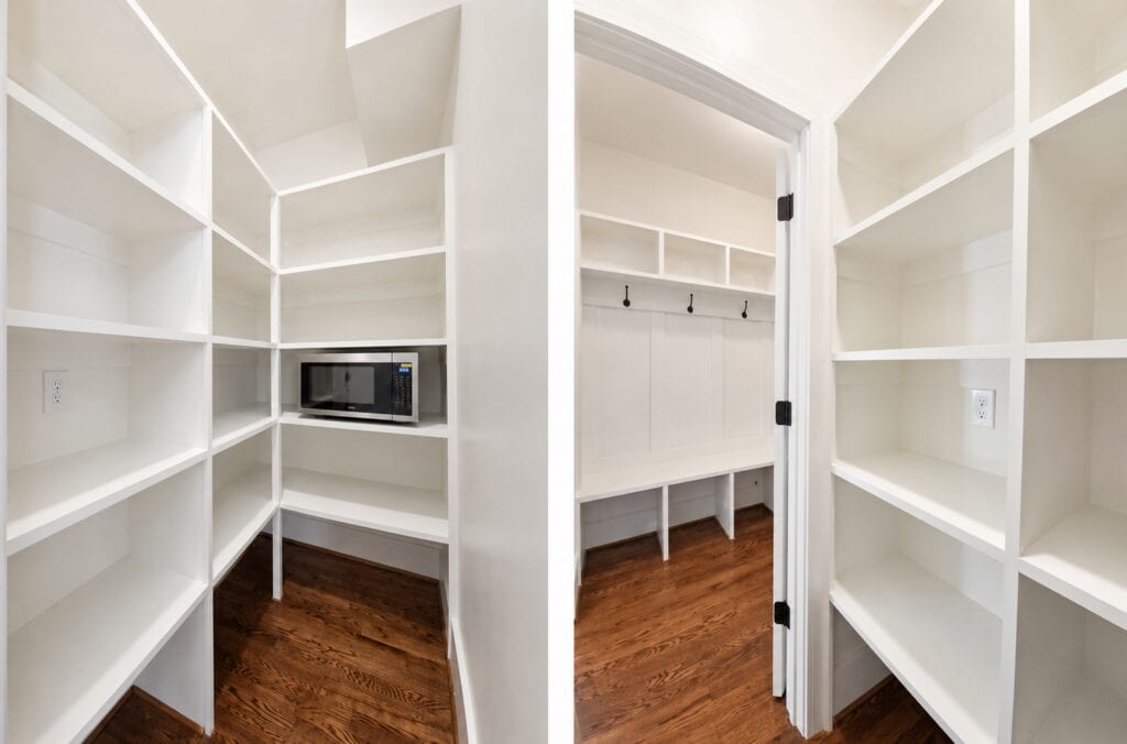 Split perspective detailing a spacious walk-in pantry with floor-to-ceiling white shelving and an integrated microwave on the left, next to a hallway mudroom bench on the right, by Travars Built Homes.