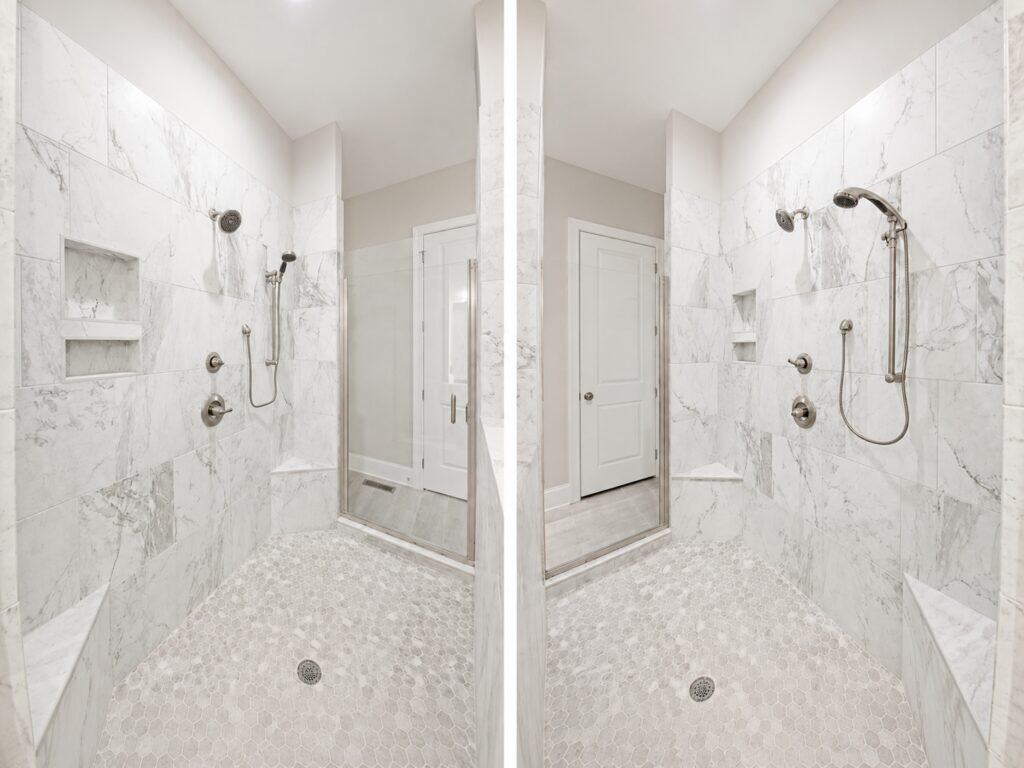 Dual-angle view inside a spacious custom walk-in shower highlighting white marble-look tiling, dual showerheads, built-in corner benches, and a hexagonal tile floor, built by Travars Built Homes.