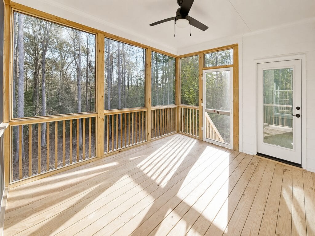Bright screened-in back porch highlighting raw timber framing, natural wood decking, a solid white ceiling with a fan, and an entry door leading back inside, crafted by Travars Built Homes.