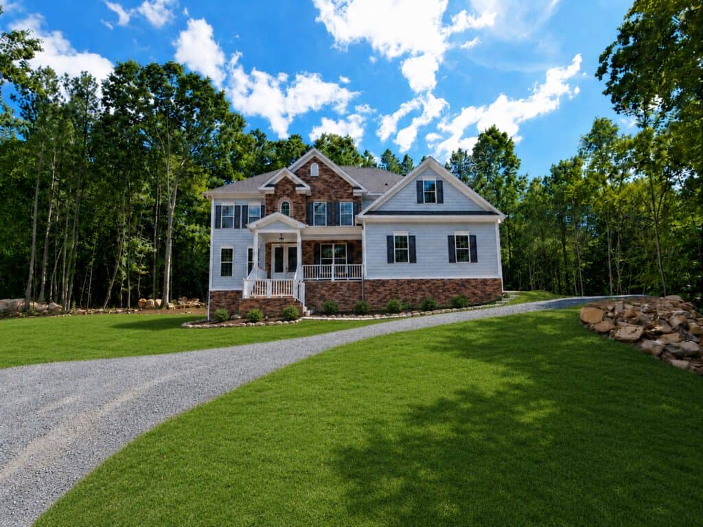 Stunning custom home exterior showcasing light blue lap siding, extensive multi-tonal stacked stone veneer across the lower facade and center gable, dark shutters, and a welcoming white front porch, built by Travars Built Homes.