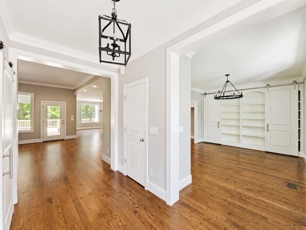 Custom home interior framing a bright entryway that seamlessly flows past an elegant dining room with sliding barn doors and into a spacious open-concept living area, built by Travars Built Homes.