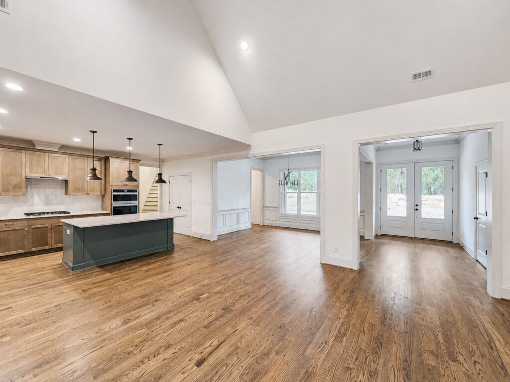 Expansive custom open floor plan viewing from the kitchen into a vaulted living area and separate dining space, highlighted by rich oak hardwood flooring throughout, crafted by Travars Built Homes.
