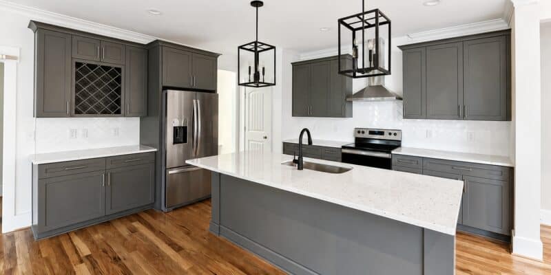 Custom kitchen design featuring sophisticated dark gray shaker cabinets, a built-in wine rack, a matching center island with a white sink, and stylish geometric black pendant lights, crafted by Travars Built Homes.
