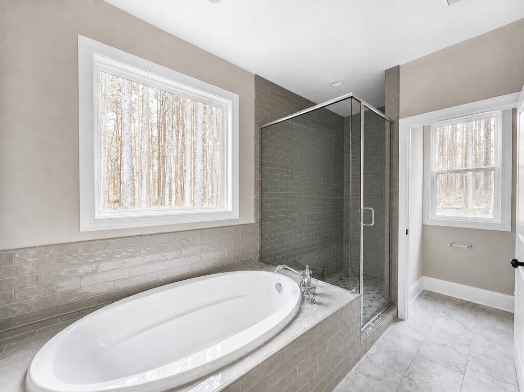 Luxury custom master bathroom showcasing a built-in soaking tub with a gray subway tile surround, adjacent to a large glass-enclosed walk-in shower with matching tile, built by Travars Built Homes.