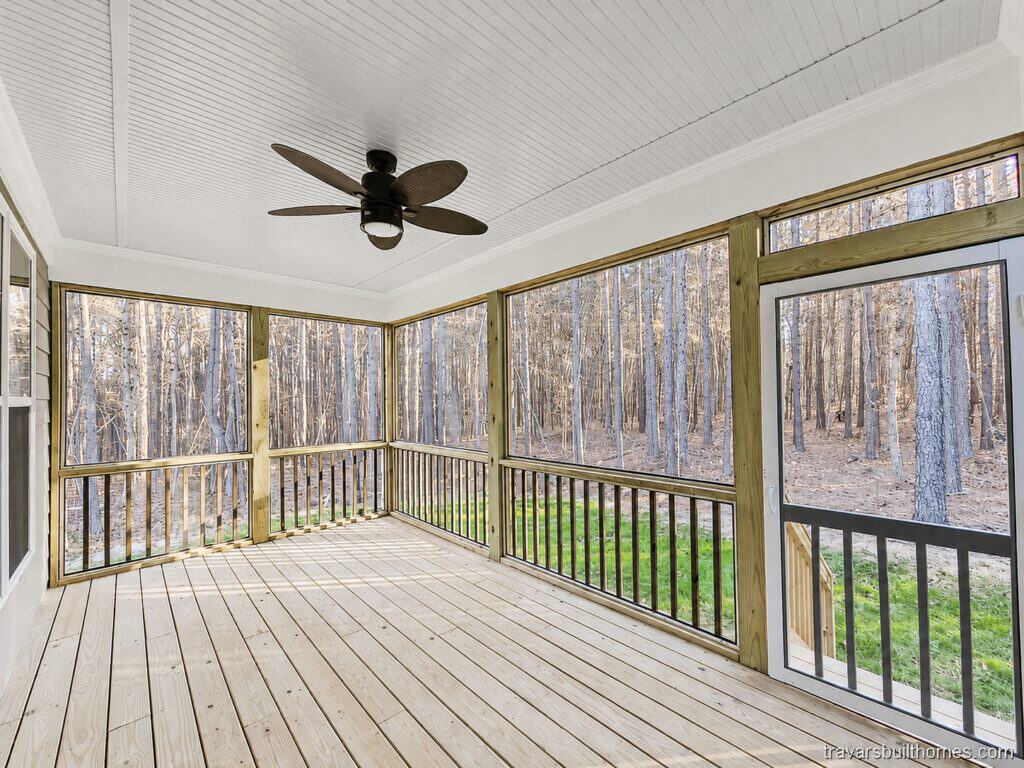 Custom screened-in back porch featuring natural wood decking, black metal railings, a white beadboard ceiling with a tropical-style fan, and a screen door leading to the backyard, built by Travars Built Homes.