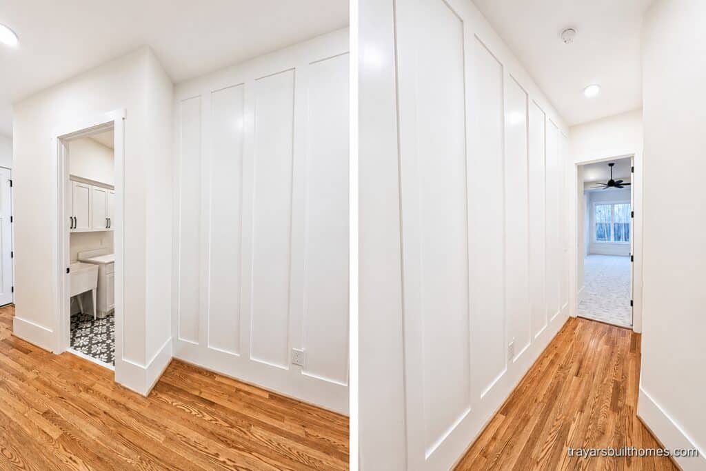 Bright custom home hallway featuring warm hardwood floors, an elegant floor-to-ceiling white paneled accent wall, and doorways leading to a laundry room and bedrooms, crafted by Travars Built Homes.