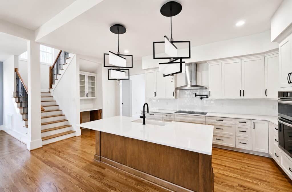 Beautiful custom kitchen design highlighting bright white cabinetry, a white subway tile backsplash, a dark-stained wood island with quartz countertops, and unique geometric black pendant lights, built by Travars Built Homes.