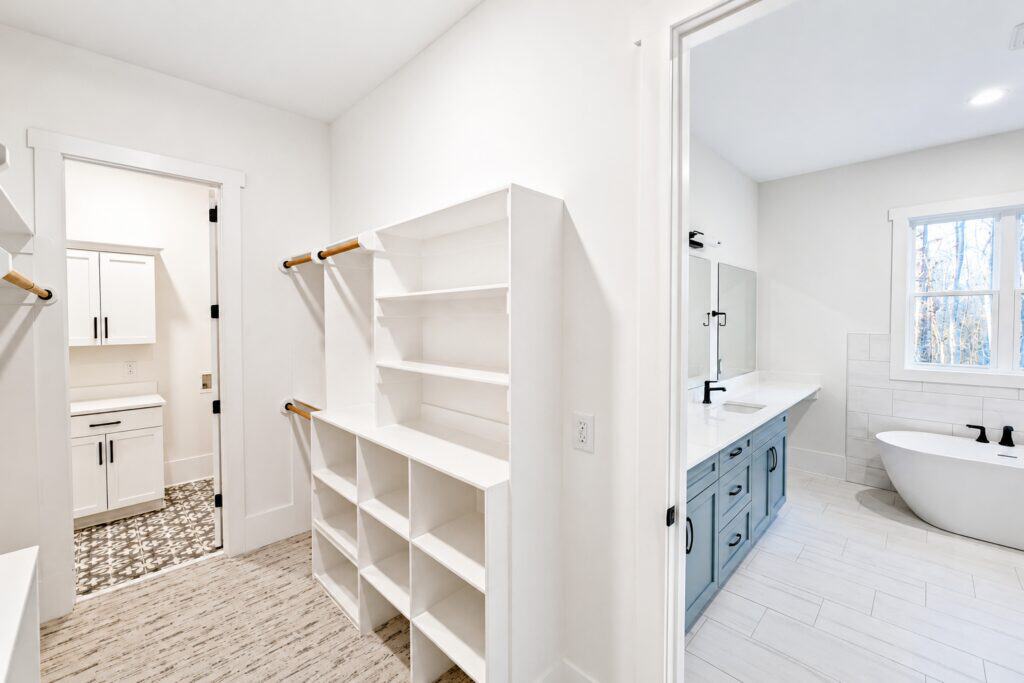 Custom home master suite layout showing a walk-in closet with built-in white shelving, connecting seamlessly to a luxury bathroom with a light blue dual vanity, built by Travars Built Homes.