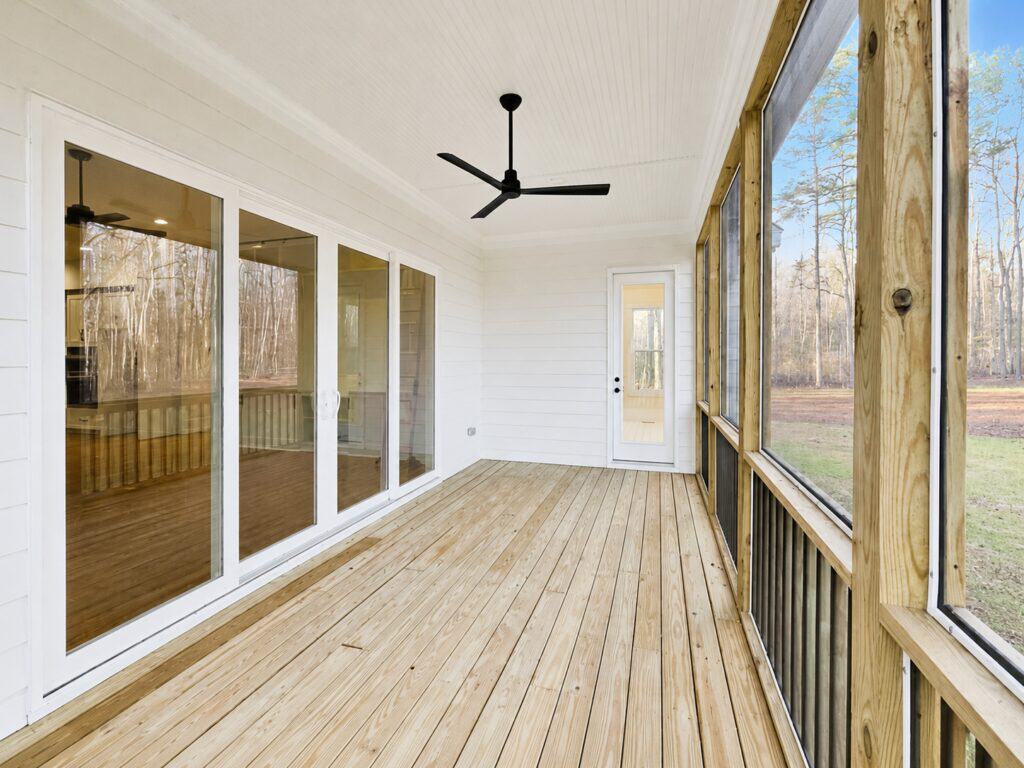 Custom home screened-in porch featuring natural wood decking, a white beadboard ceiling with a black ceiling fan, and large sliding glass doors connecting the outdoor and indoor living spaces, built by Travars Built Homes.