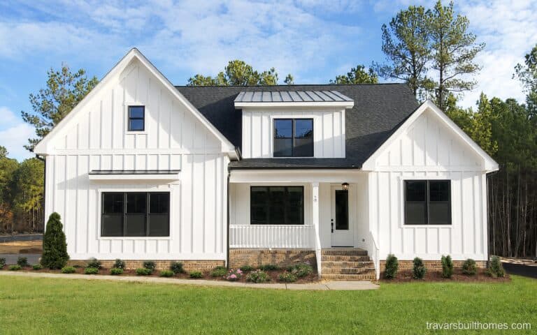 Beautiful custom modern farmhouse exterior featuring bright white board-and-batten siding, contrasting black window frames, a classic brick foundation, and a covered front porch, built by Travars Built Homes.