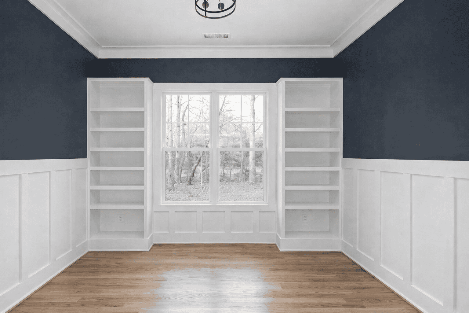 Bright home office featuring custom white built-in bookshelves and large window with garden view.
