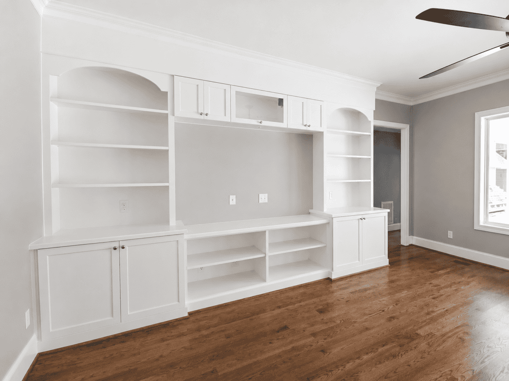 Southern farmhouse great room with white built-in entertainment center, open shelving, lower cabinets, hardwood floors, and ceiling fan by Travars Built Homes.